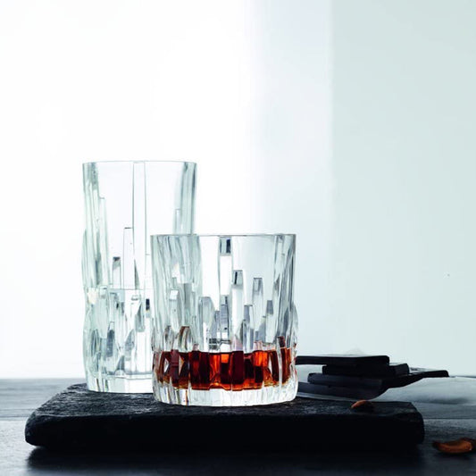 Two clear glass tumblers with a dark liquid on a dark surface and light background